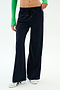 A person wears SPLITS59 Brynn Airweight Pant in Indigo, featuring a comfortable nylon-spandex blend, paired with a green long-sleeve top and white sneakers, standing against a plain white background.