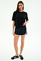 A woman stands against a white background wearing the SPLITS59 Djuna Oversized Jersey Tee in black, paired with black athletic shorts with white trim and black sneakers.