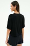 A woman faces away, wearing the SPLITS59 Djuna Oversized Jersey Tee in black with black athletic shorts featuring white trim against a light background—ideal gym workout attire.
