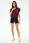 A woman with straight brown hair and a neutral expression stands against a white background wearing the SPLITS59 Evie Fleece Sleeveless Polo in Dark Cherry, paired with black shorts and white sneakers featuring maroon stripes.