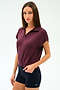 A woman with straight brown hair wears the SPLITS59 Evie Fleece Sleeveless Polo in Dark Cherry and black fitted spandex shorts against a plain light background.
