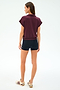 A woman stands facing away in a SPLITS59 Evie Fleece Sleeveless Polo in Dark Cherry, paired with black shorts and beige sneakers with maroon stripes, set against a plain light background.