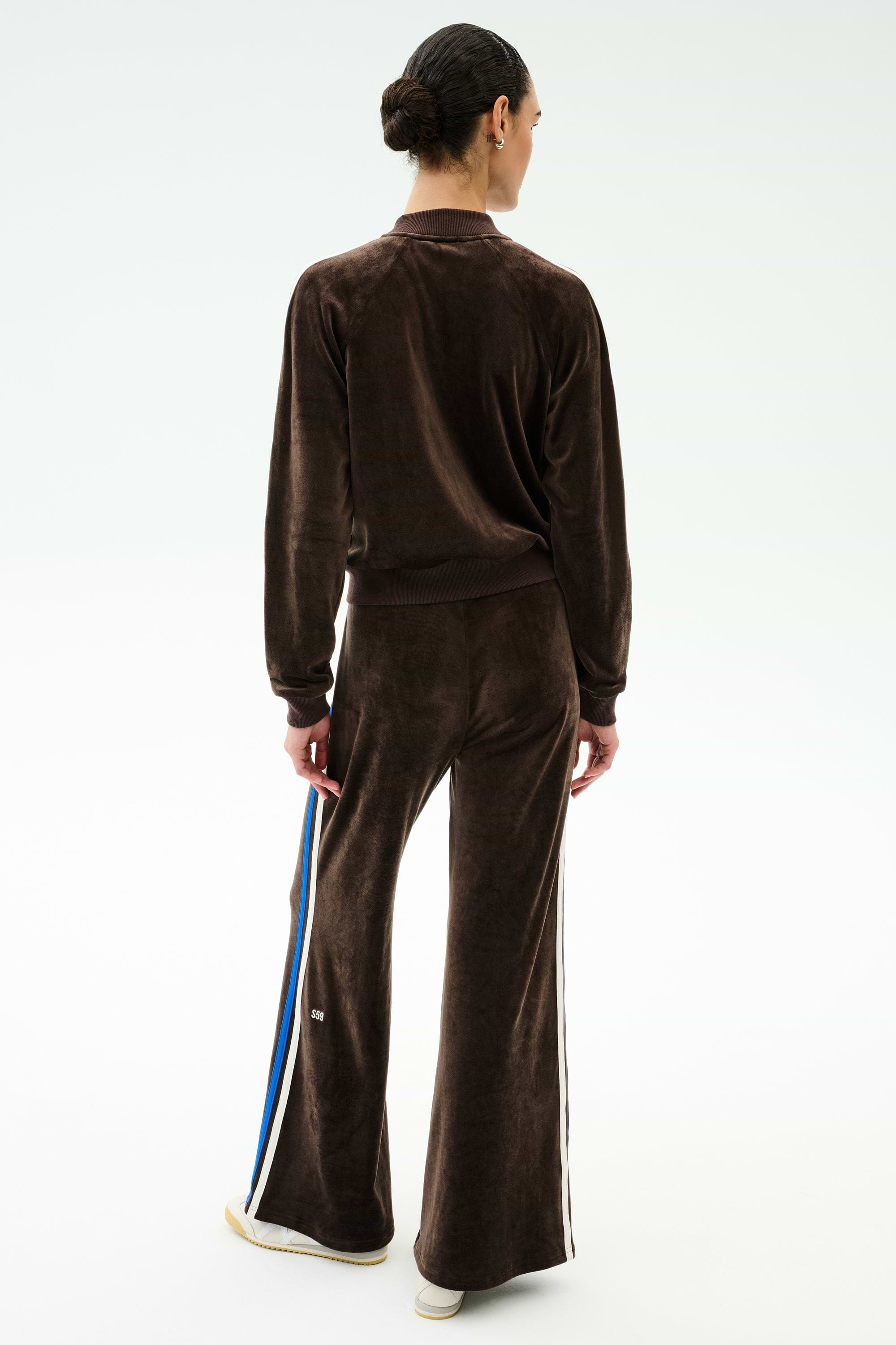 Person faces away from the camera wearing SPLITS59’s Heritage Velour Pant in Dark Chocolate/Classic Blue, a flared wide-leg style with side stripes, set against a plain white background.