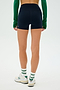 Person in a green long-sleeve top, SPLITS59 Ella Airweight High Waist Short 3.5", white sneakers, and socks with green stripes, standing with their back to the camera on a white background.