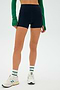 A person in a green long-sleeve top wears SPLITS59's Ella Airweight High Waist Short 3.5" in Indigo/White, standing with legs apart in white sneakers and green-striped socks against a plain white background.