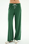 A person wearing SPLITS59 Willow Airweight Wide Leg pants in Arugula/White and white sneakers with black stripes stands against a plain white background.