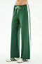 A person wears SPLITS59 Willow Airweight Wide Leg pants in Arugula/White, featuring white side stripes and a drawstring waist, paired with white sneakers with black stripes, standing against a plain background.