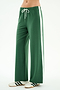 A person wears SPLITS59 Willow Airweight Wide Leg pants in Arugula/White, featuring white side stripes and a drawstring waist, paired with white sneakers with black stripes, standing against a plain background.