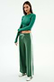 A woman stands against a white background wearing the SPLITS59 Willow Airweight Wide Leg pants in Arugula/White, paired with a fitted green spandex top and white sneakers with green accents.