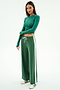 A woman stands against a white background wearing the SPLITS59 Willow Airweight Wide Leg pants in Arugula/White, paired with a fitted green spandex top and white sneakers with green accents.