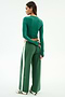 A woman faces away, wearing SPLITS59's Willow Airweight Wide Leg pants in Arugula/White and a fitted green spandex long-sleeve top, paired with white sneakers featuring black stripes.