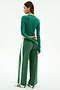 A woman faces away, wearing SPLITS59's Willow Airweight Wide Leg pants in Arugula/White and a fitted green spandex long-sleeve top, paired with white sneakers featuring black stripes.