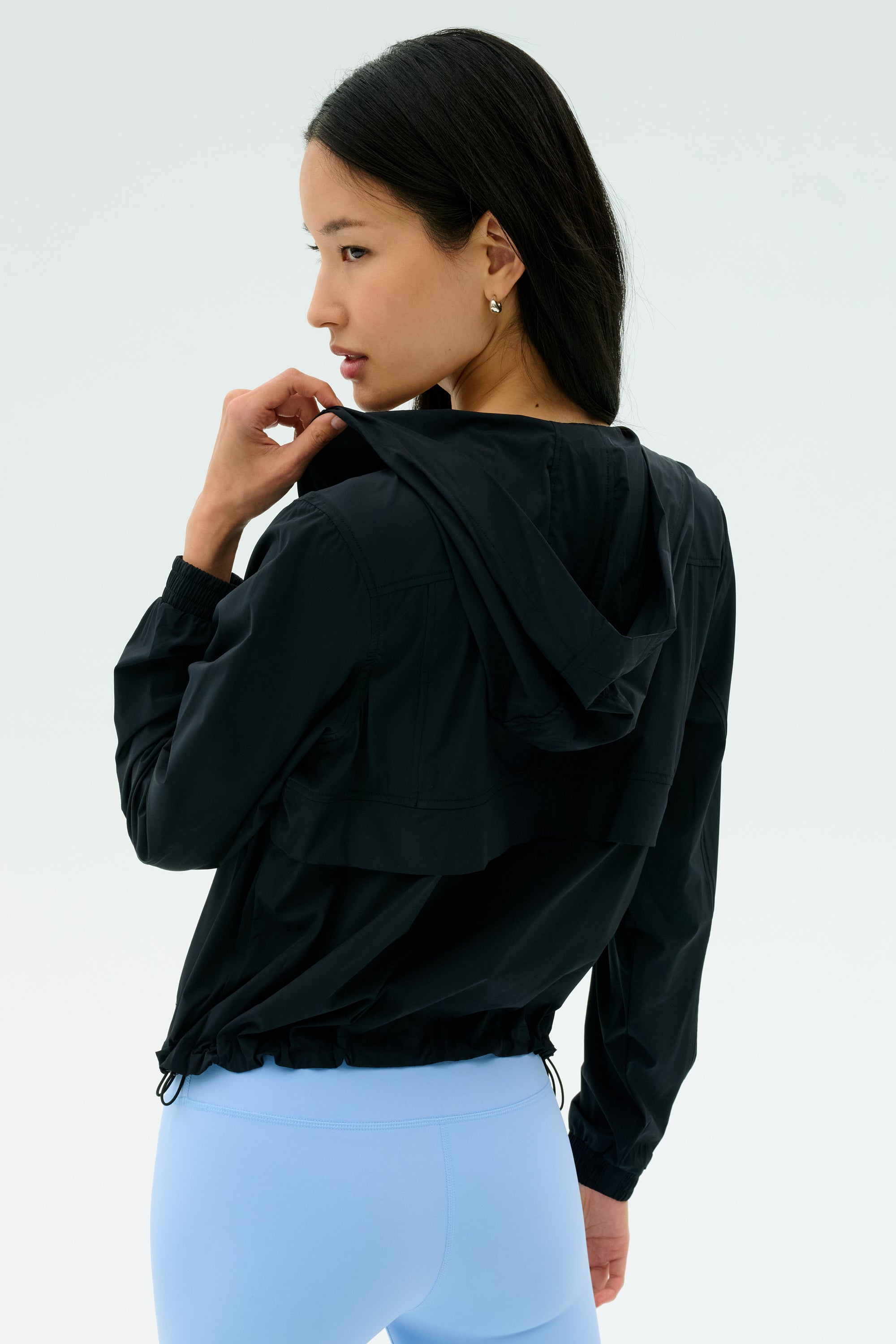 A woman wearing the SPLITS59 Megan Woven Nylon Jacket in black stands facing away, looking over her shoulder against a plain light background.