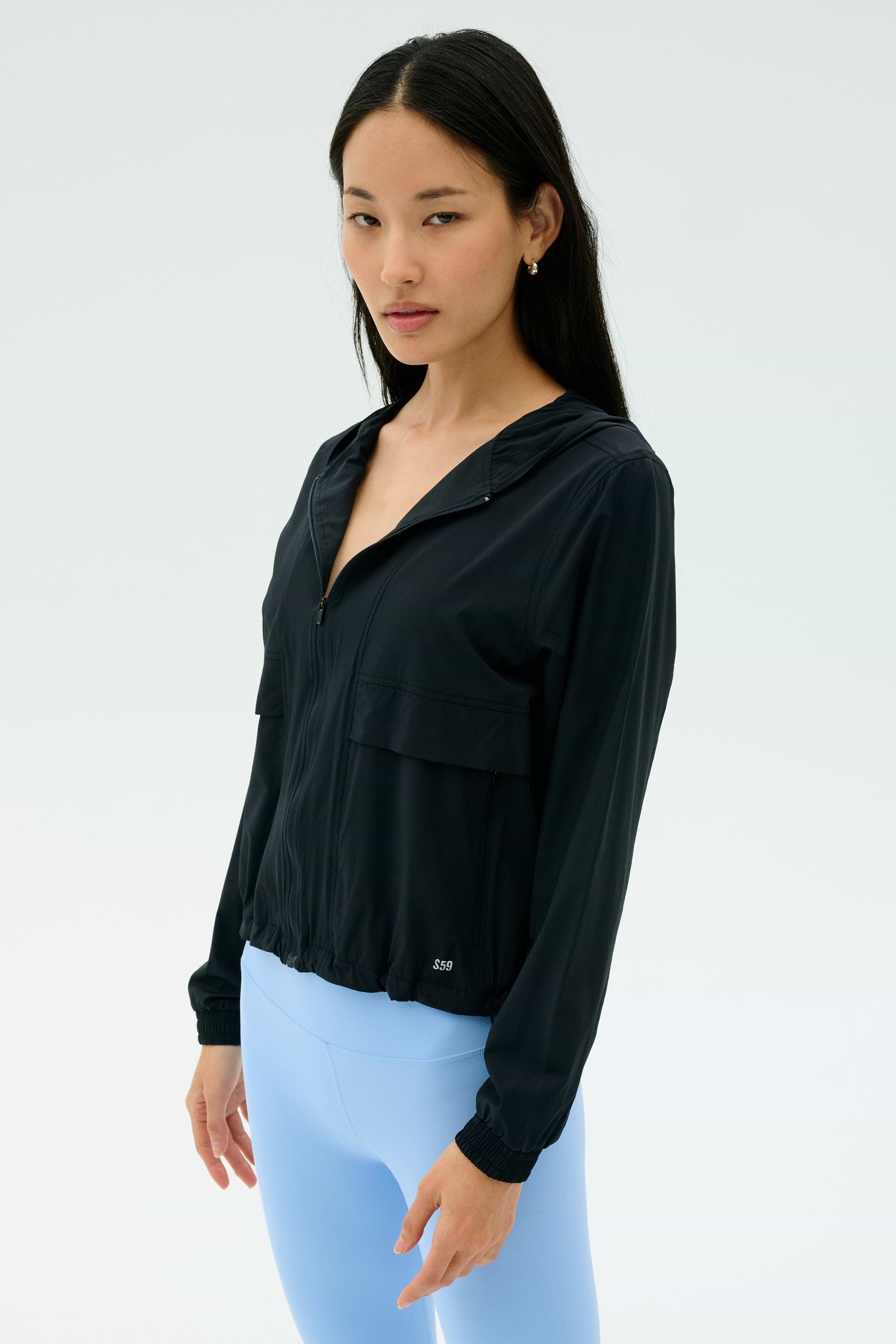A woman wears the SPLITS59 Megan Woven Nylon Jacket in black, standing against a plain, light background.
