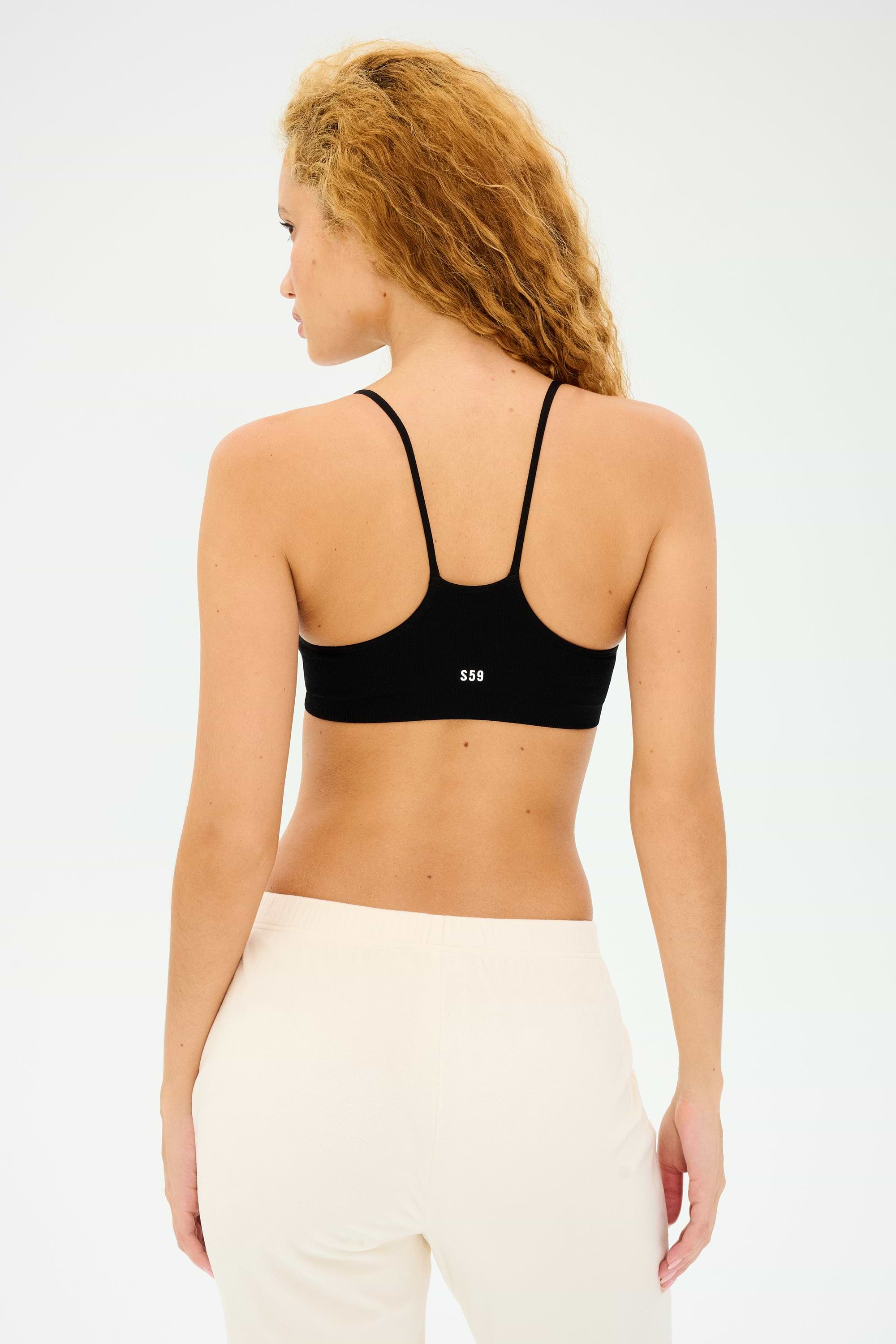 A person with curly hair models the Loren Seamless Bra in black from Splits59, paired with beige pants, facing away from the camera.
