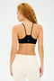 A person with curly hair models the Loren Seamless Bra in black from Splits59, paired with beige pants, facing away from the camera.
