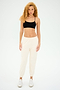 With curly hair, a person wears the Loren Seamless Bra in black and cream chafe-free pants, perfectly paired with white sneakers against a plain background.