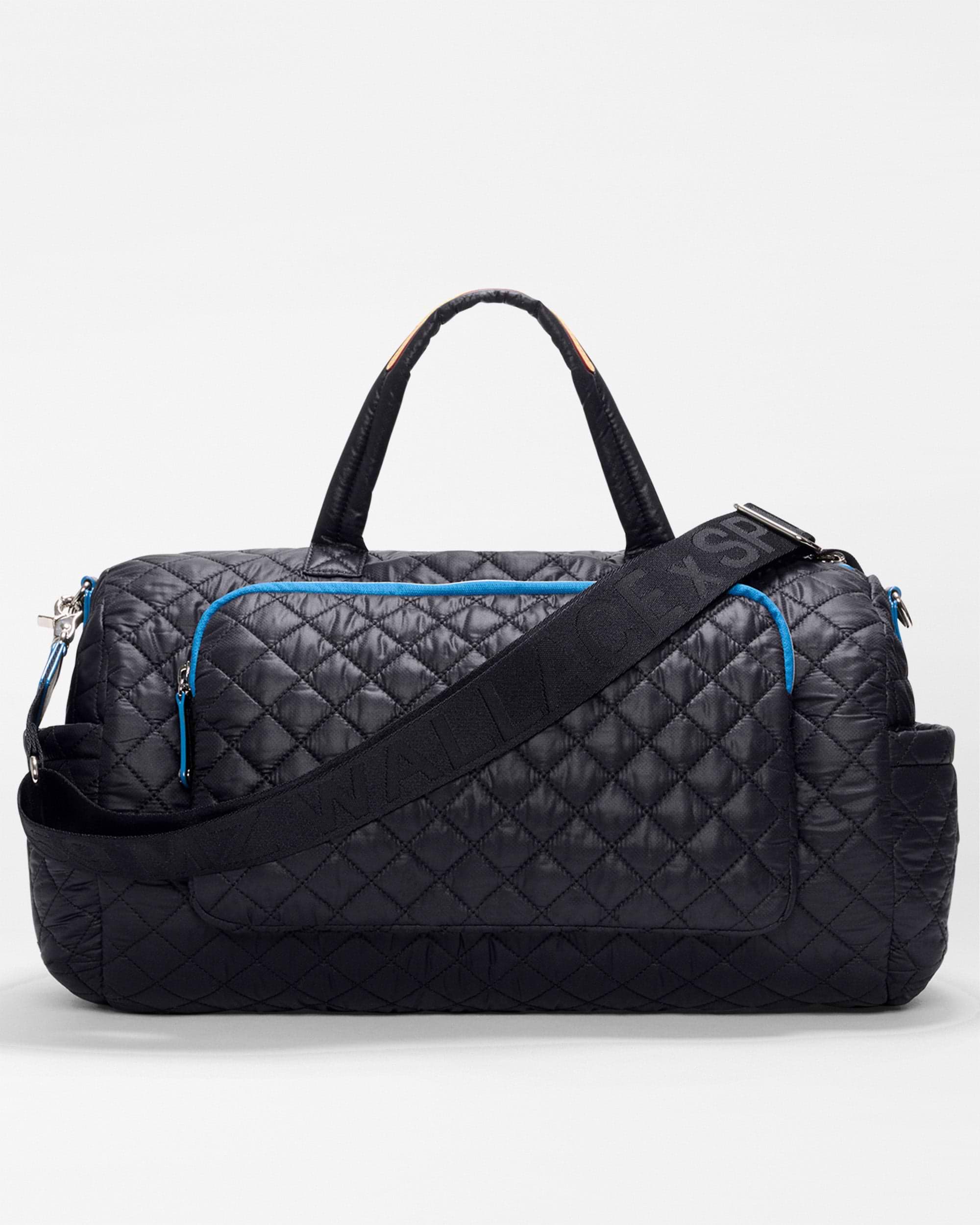 The SPLITS59 MZW x Splits59 Duffle is a black quilted bag with blue zippers, dual handles, an adjustable shoulder strap, and several exterior pockets, shown on a plain background.