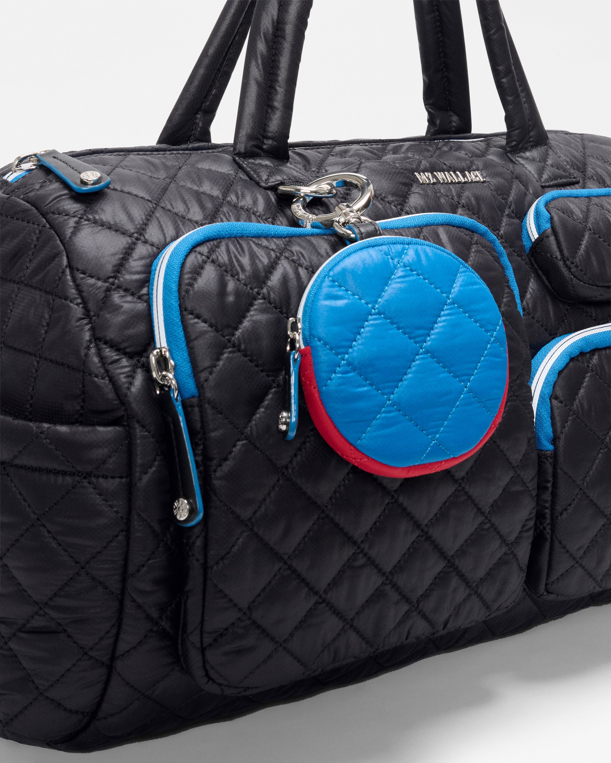 The SPLITS59 MZW x Splits59 Duffle is a black quilted bag with blue and red zipper accents, featuring a round blue quilted pouch attached to the front pocket.