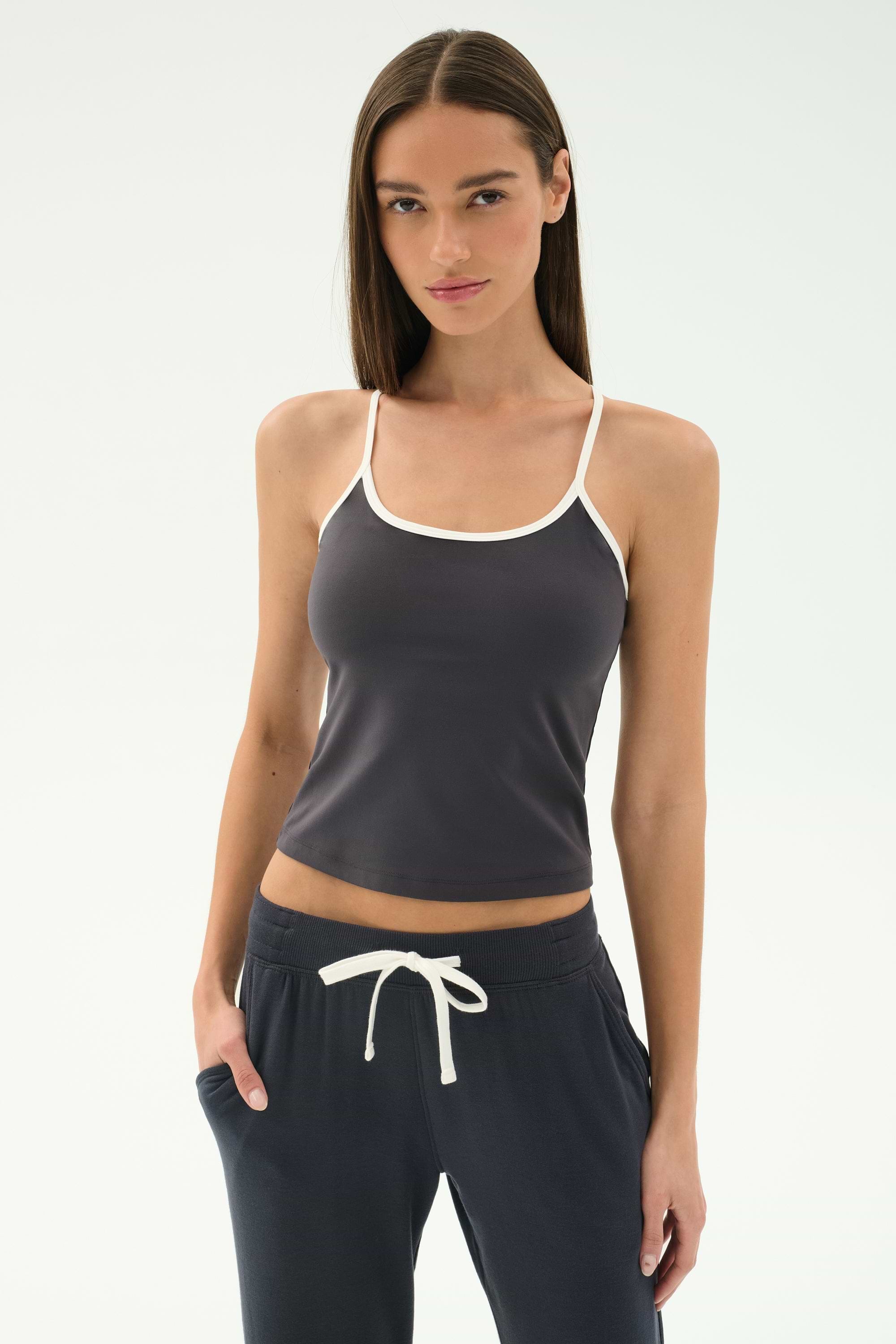 A woman in the SPLITS59 Airweight Tank - Graphite/White stands with her hands in her pockets, wearing matching drawstring pants and ready for Pilates against a plain background.