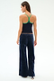 A woman stands with her back to the camera, wearing a navy racerback tank top with green trim and SPLITS59 Heritage Velour Pant - Indigo/White, featuring soft polyester-spandex fabric and a relaxed fit.