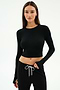 A woman wears the SPLITS59 Louise Rib Long Sleeve Crop in black, paired with black drawstring pants, standing against a plain white background.