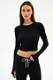 A woman wears the SPLITS59 Louise Rib Long Sleeve Crop in black, paired with black drawstring pants, standing against a plain white background.