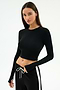 A woman wears the SPLITS59 Louise Rib Long Sleeve Crop in black, paired with black athletic pants featuring a white drawstring and side stripe, standing against a plain white background.
