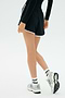 A person stands against a plain light background wearing a black long-sleeve spandex top, SPLITS59 Megan Woven Nylon Run Short in black, white socks, and white sneakers.