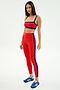 A woman wears the SPLITS59 Clare High Waist Rigor 7/8 leggings in Lotus Red/Cobalt with a matching crop top and blue sneakers, standing against a white background—ideal athletic style for your next workout.