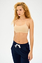 A person with curly hair in a beige Loren Seamless Bra by Splits59 and dark blue chafe-free drawstring pants, ideal for gym workouts, appears against a plain backdrop.