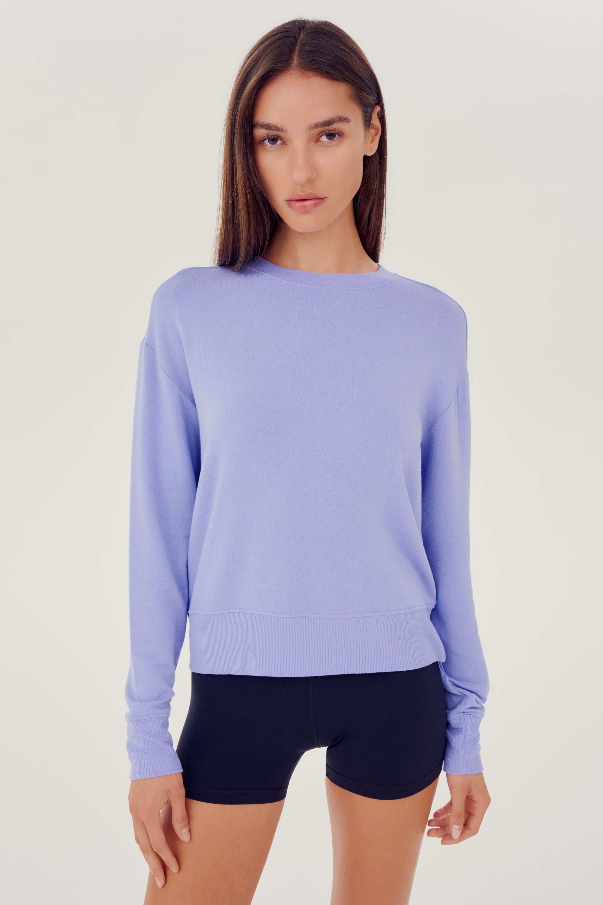 Front view of woman with dark brown hair wearing a light purple crewneck sweatshirt and black shorts
