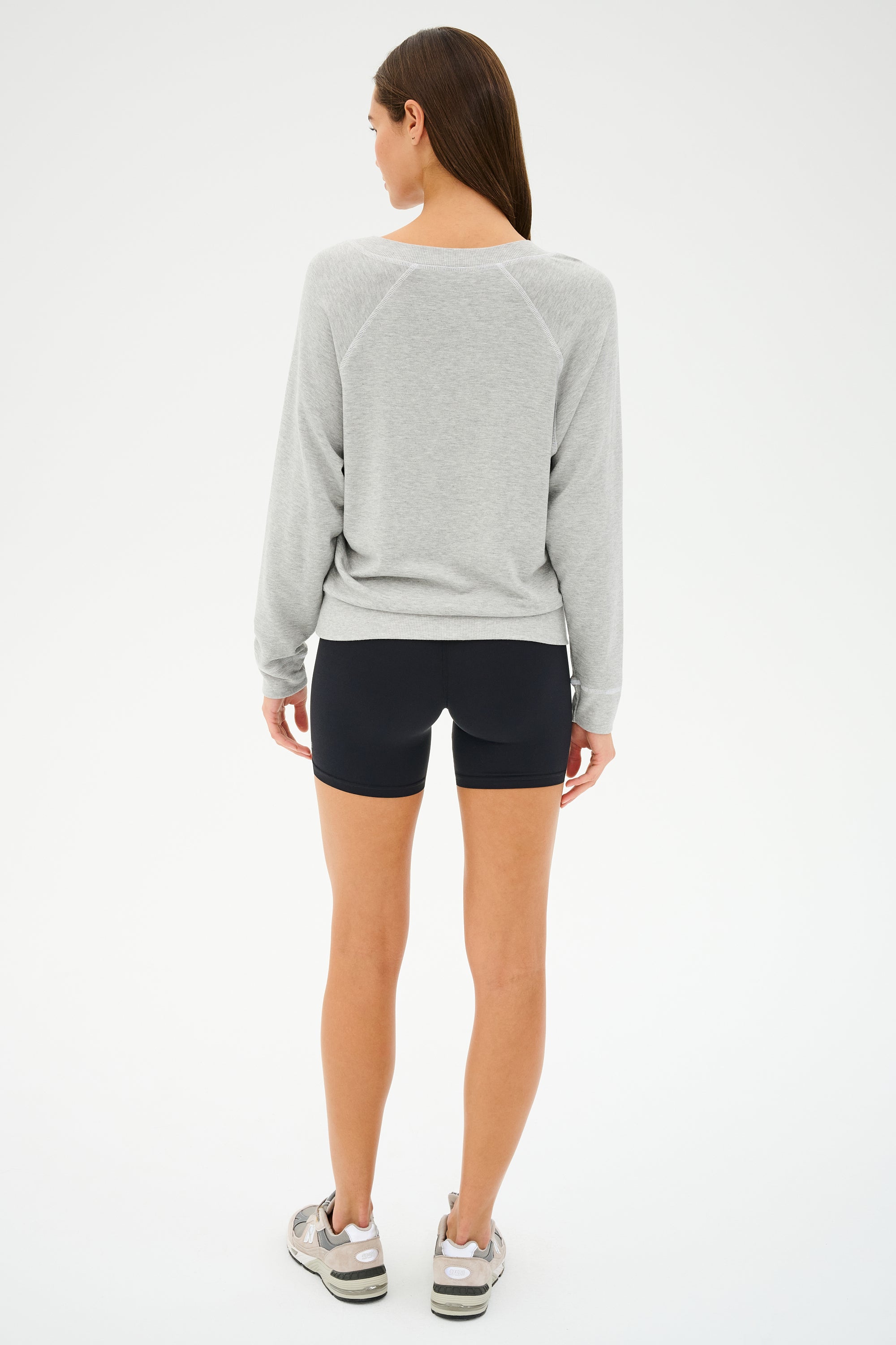 A person wearing a versatile pullover, SPLITS59's Bennie Fleece V-Neck Sweatshirt in Heather Grey/White, black shorts, and sneakers is standing and facing away.