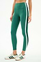 A person stands against a plain background wearing SPLITS59 Bianca High Waist Rigor 7/8 leggings in Arugula/White, which feature white and dark green side stripes, paired with white sneakers with green stripes.