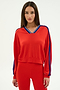 A woman stands against a plain background wearing the SPLITS59 Ellie Fleece V Neck Sweatshirt in Lotus Red/Cobalt, featuring blue sleeve stripes and crafted from a comfortable modal-spandex blend.