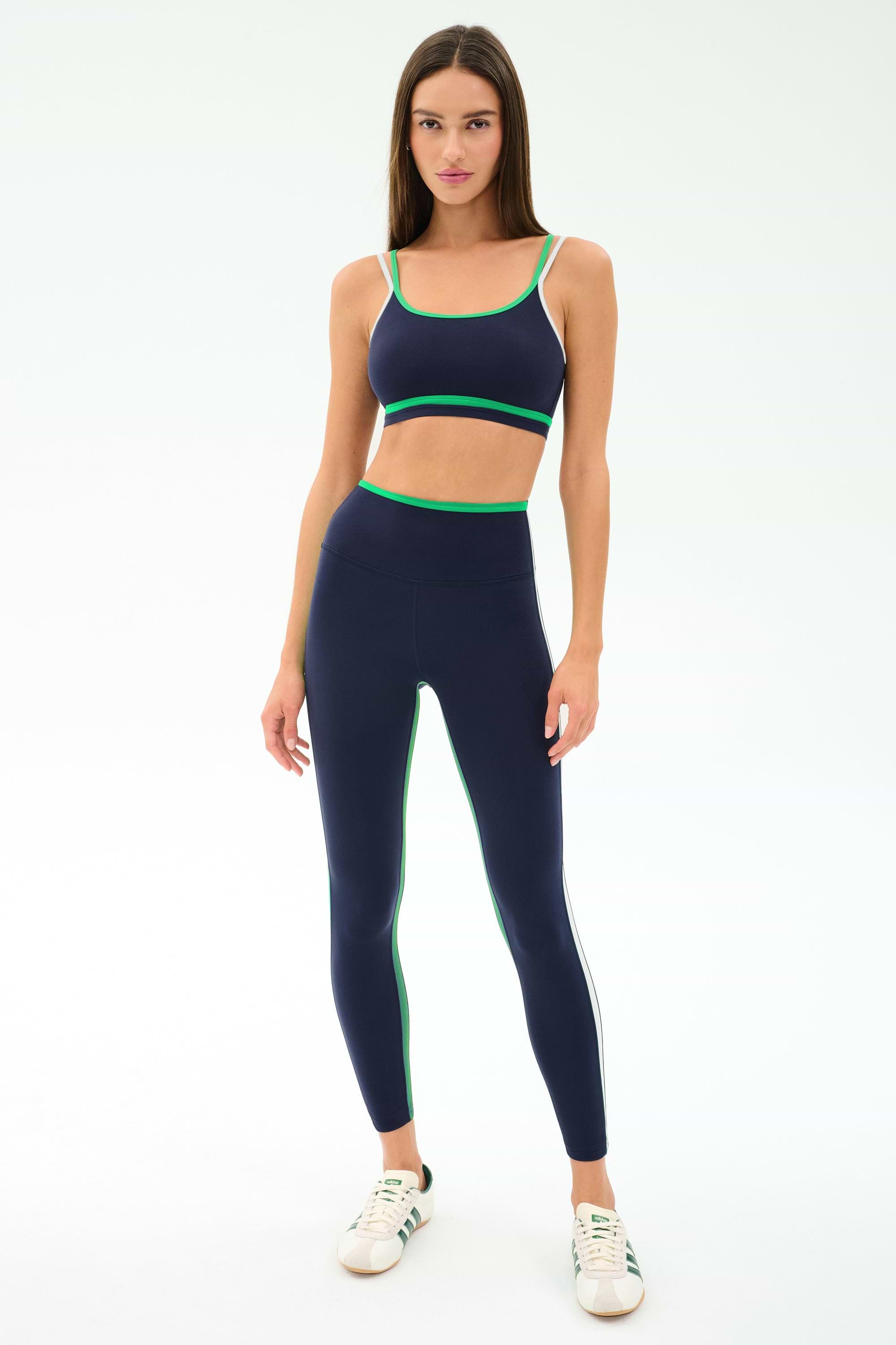 A woman faces forward wearing the SPLITS59 Eva Rigor Double Strap Bra in Indigo/Spearmint, paired with matching high-waisted leggings and white sneakers, set against a plain light background.