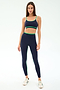 A woman faces forward in SPLITS59's Sam High Waist Rigor 7/8 leggings in Indigo/Spearmint with a matching sports bra and white sneakers, set against a plain white background.
