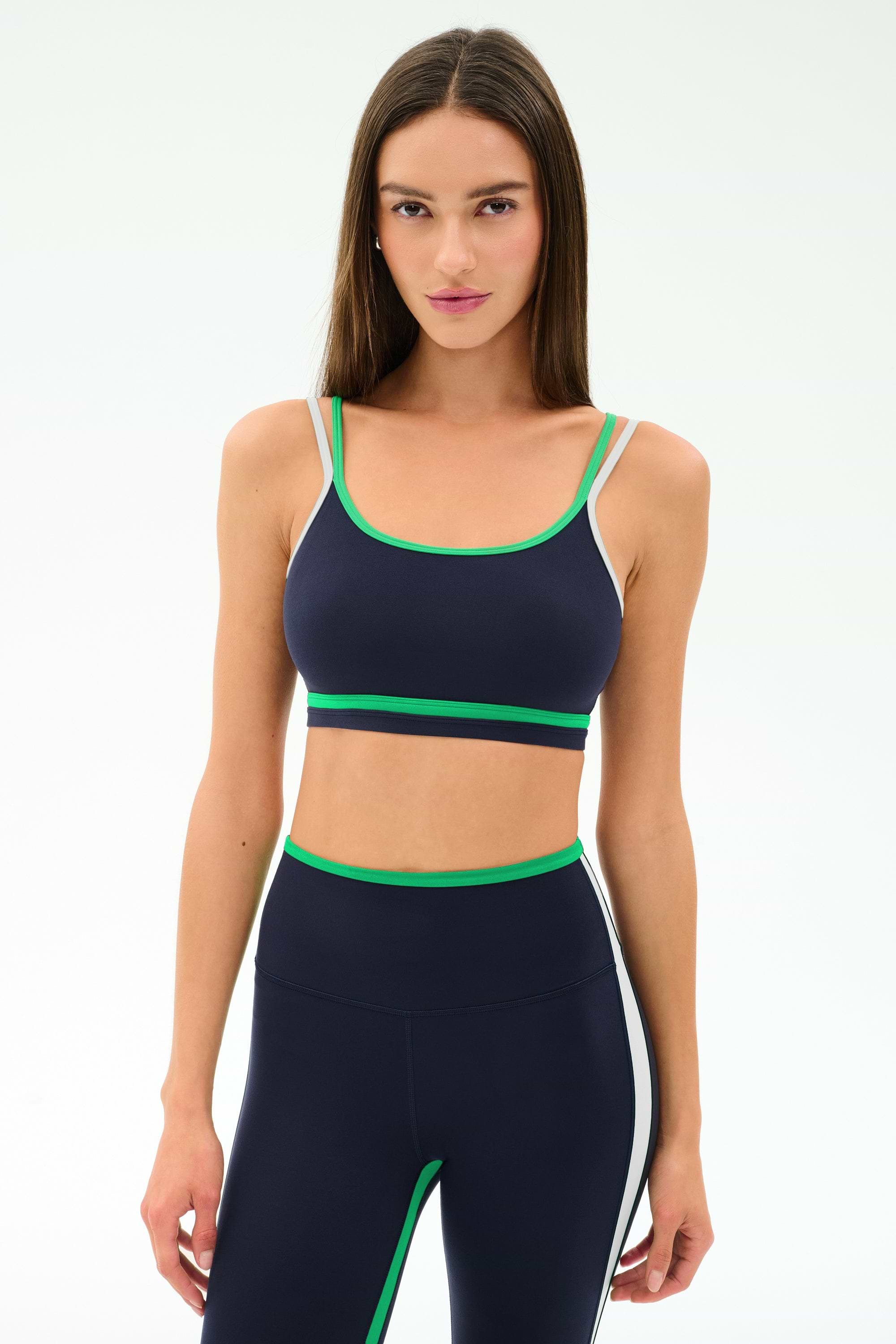 A woman stands against a white background wearing the SPLITS59 Eva Rigor Double Strap Bra in Indigo/Spearmint, paired with matching leggings, ready for her workout.