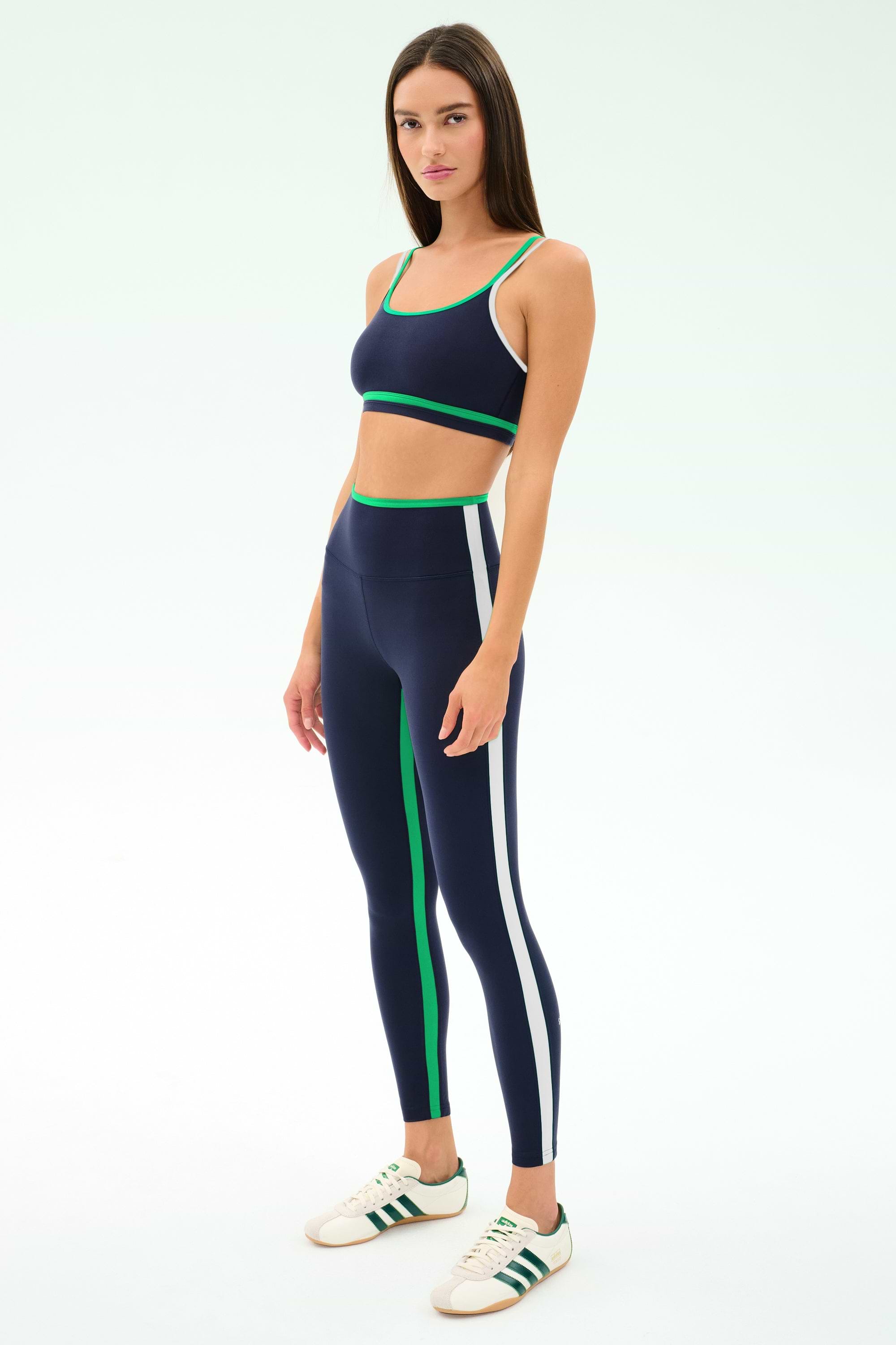 A woman wears the SPLITS59 Sam High Waist Rigor 7/8 leggings in Indigo/Spearmint with a matching sports bra and white sneakers, standing against a plain light background.