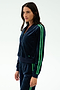 A woman models the SPLITS59 Heritage Velour Bomber in Indigo/Grass, featuring green stripes on navy blue velour, combining sporty comfort with yoga-inspired style against a white background.