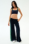 Model in SPLITS59 Heritage Velour Pant in Indigo/Grass, featuring soft navy velour with green stripes and a modern ankle-length wide leg, poses against a plain white background.