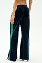 A person is seen from behind wearing the SPLITS59 Heritage Velour Pant in Indigo/Grass, featuring navy velour fabric with green side stripes and a relaxed wide-leg fit that flares stylishly at the ankle, against a plain white background.