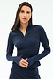 A woman with long dark hair wears the SPLITS59 Stevie Active Rib Half Zip Waist Length top in Heather Indigo, standing against a plain light background.