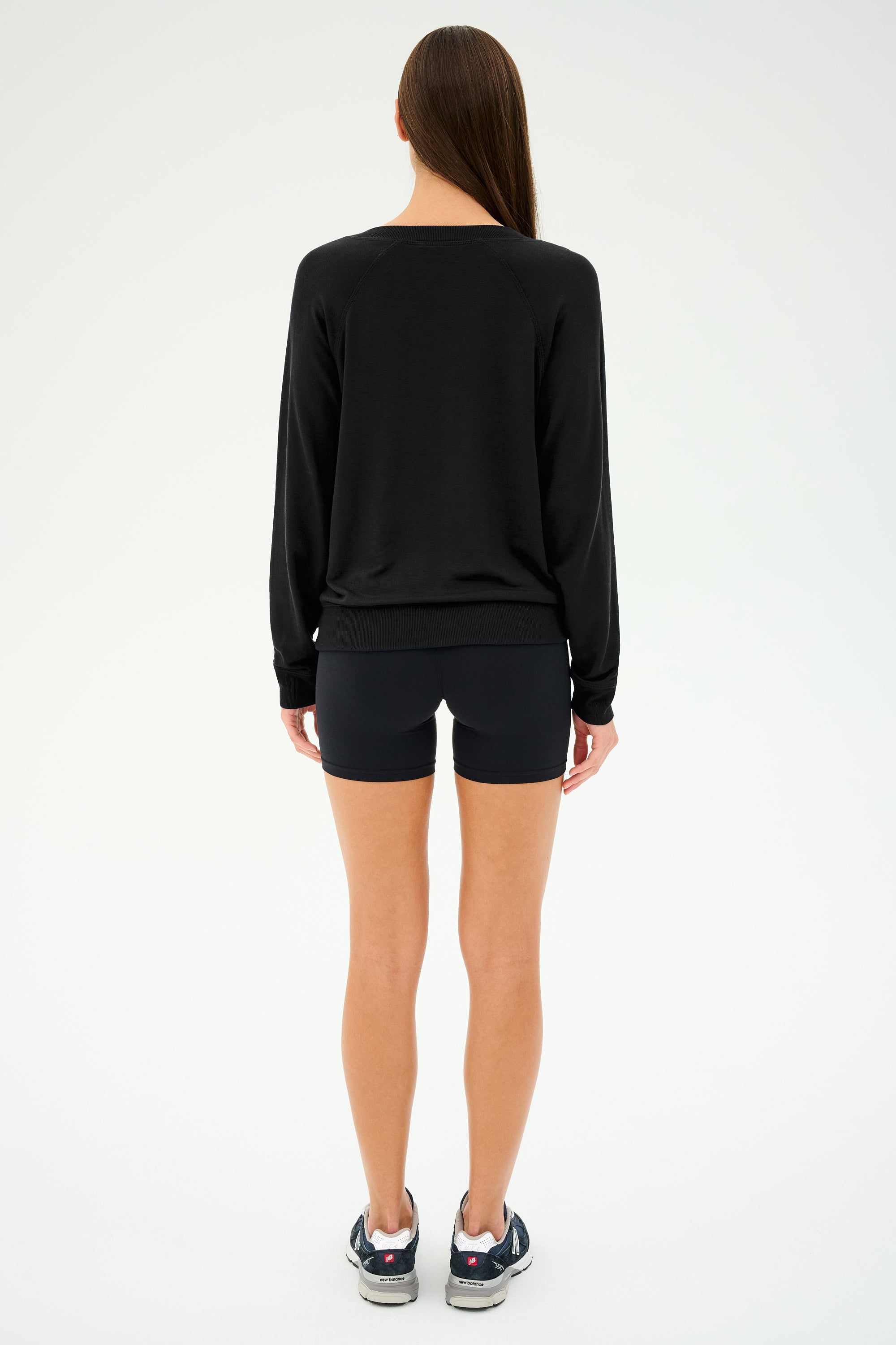 A woman stands with her back to the camera wearing a SPLITS59 Bennie Fleece V-Neck Sweatshirt in sleek black, paired perfectly with matching shorts and sneakers.