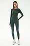 A woman faces forward, wearing the SPLITS59 Airweight Lite LS Waist Length in Military— a long-sleeve green top made from soft nylon-spandex—paired with matching leggings and white sneakers against a plain white background.