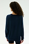A person with curly hair stands facing away, wearing the SPLITS59 Andie Fleece Sweatshirt in Indigo and black shorts against a plain, light background.