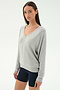 A woman in the SPLITS59 Bennie Fleece V Neck Sweatshirt in Heather Grey/White, made in Los Angeles, stands against a plain white background wearing black shorts.