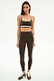 A woman faces forward wearing the SPLITS59 Bianca Rigor Bra in Dark Chocolate/White with matching high-waisted leggings and brown Nike sneakers—an ideal gym workout outfit.