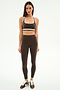 A woman stands facing forward against a white background, wearing SPLITS59's Bianca High Waist Rigor 7/8 leggings in Dark Chocolate/White and a matching sports bra.