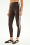 A person wears SPLITS59's Bianca High Waist Rigor 7/8 leggings in Dark Chocolate/White with two white stripes, paired with brown and white sneakers, standing against a plain white background.